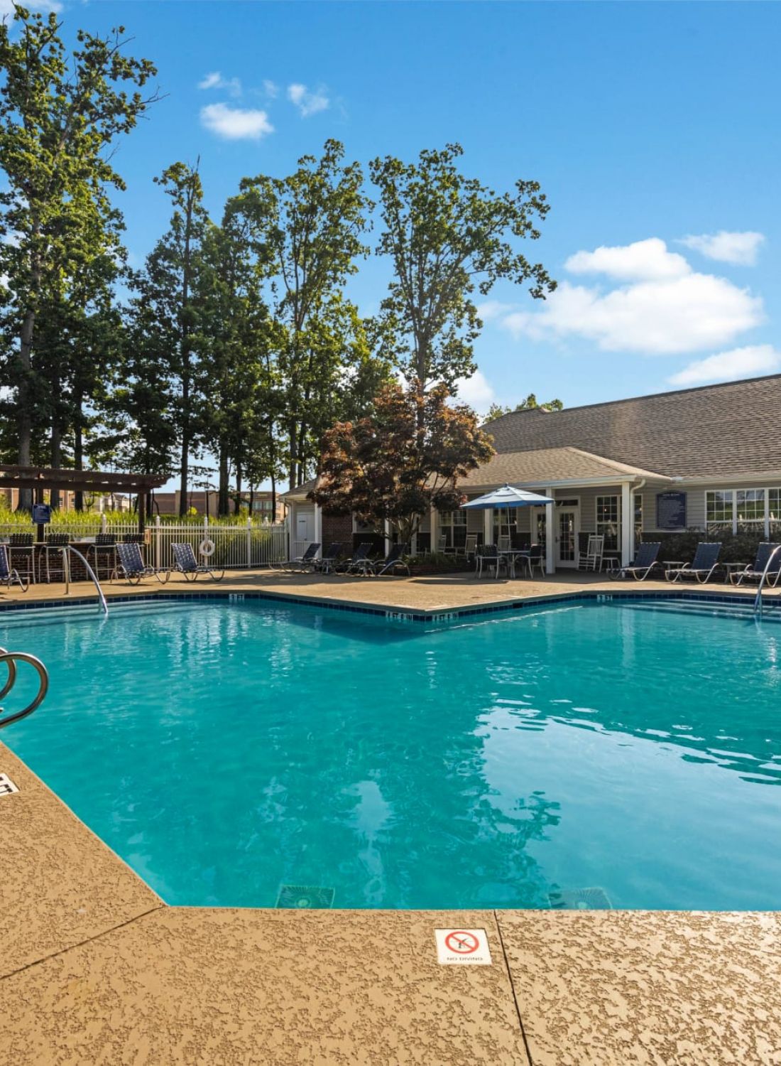 Outdoor swimming pool with lounge chairs, umbrellas, and a building in the background on a sunny day.