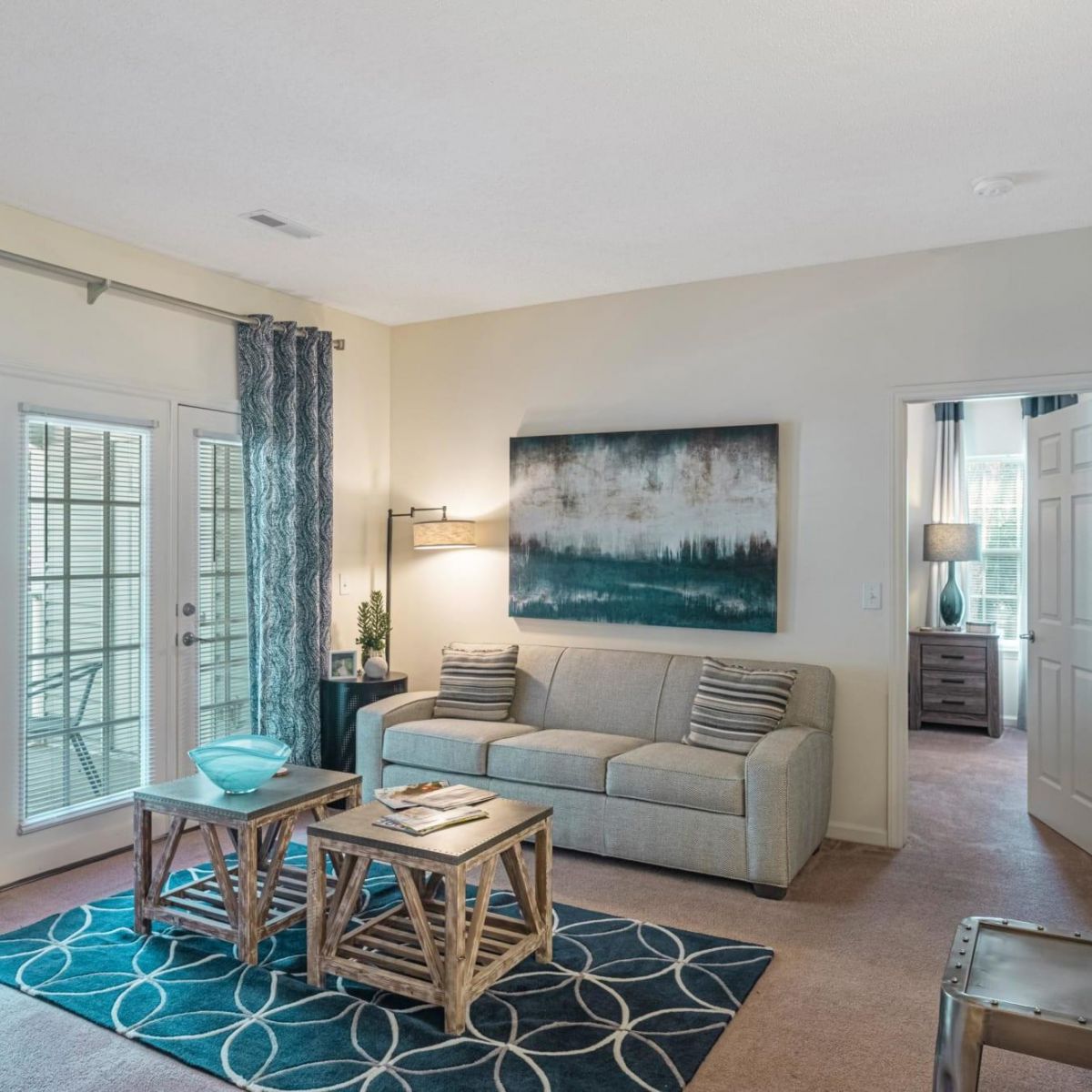 Bright living room with a beige sofa, blue accents, and glass doors leading to a balcony.