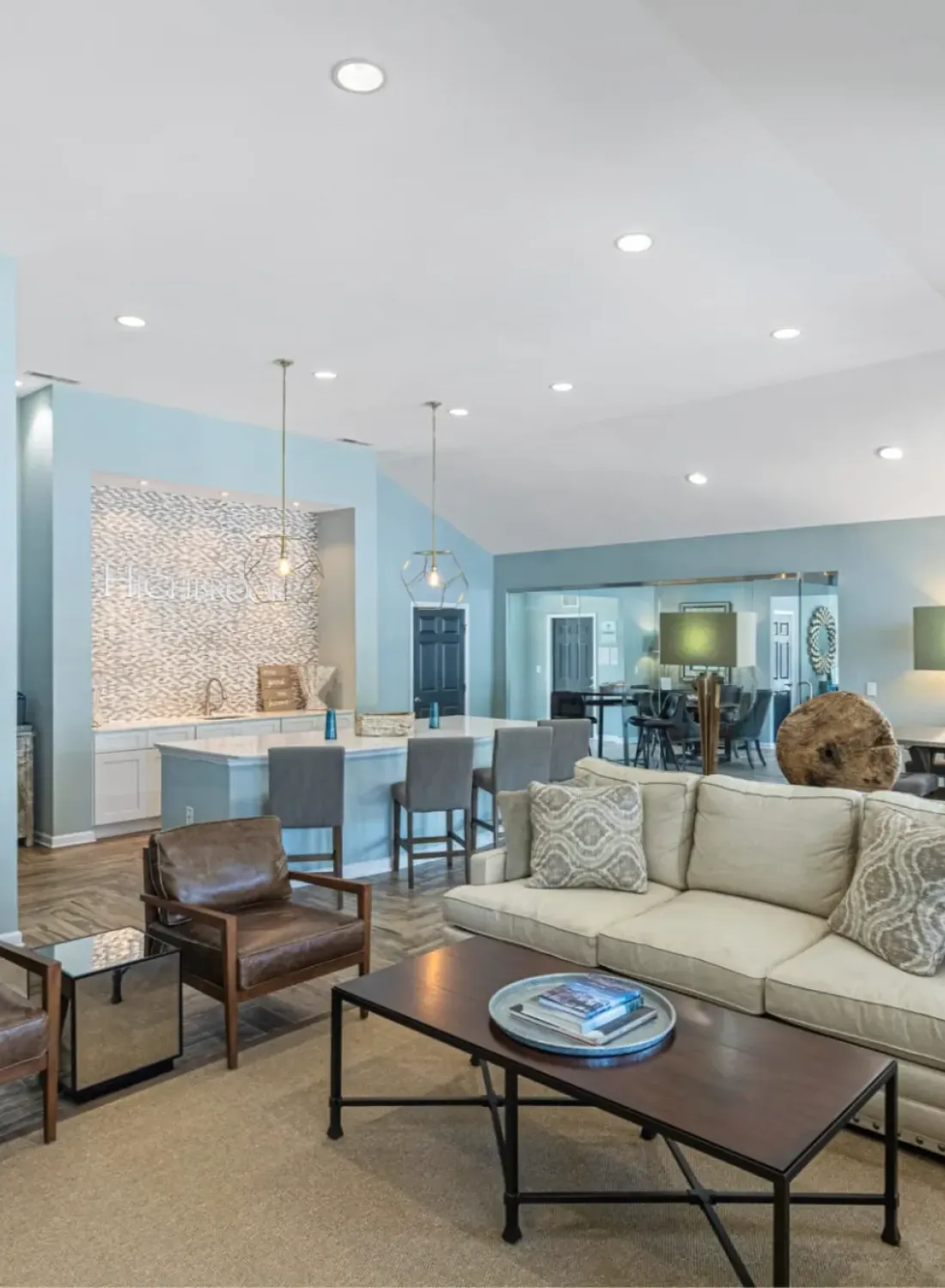 Modern living room with blue walls, brown chairs, beige sofa, and decorative wall art, leading to dining area.